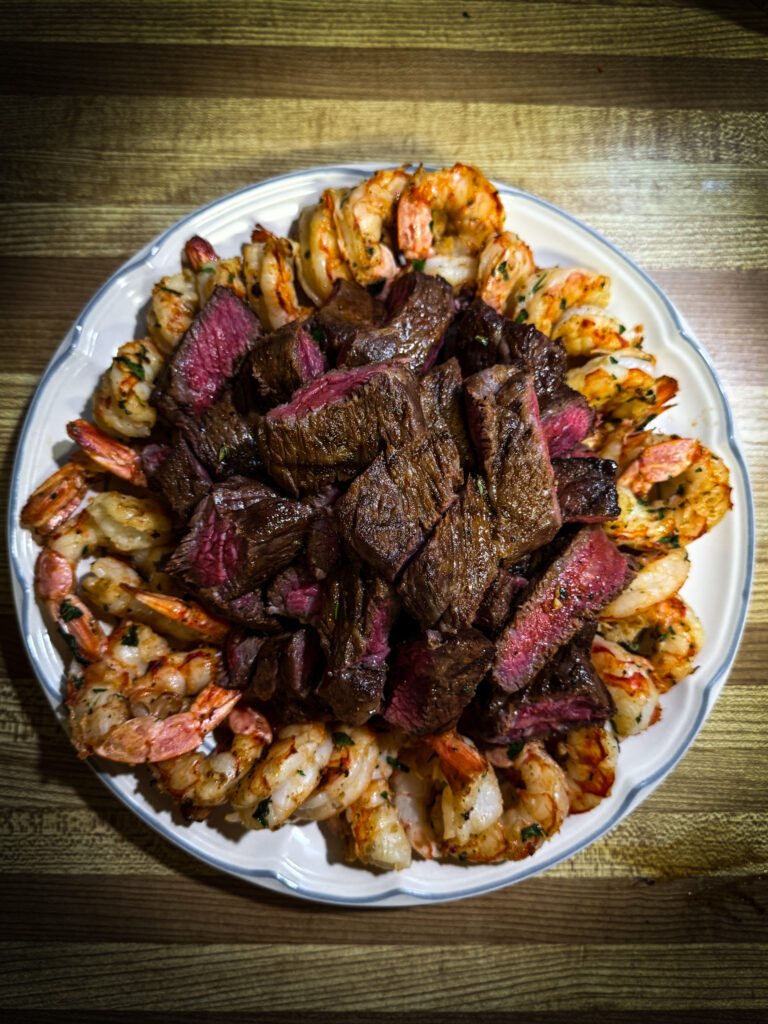 Close-up of grilled Denver steak slices with seared shrimp and compound butter melting over the top