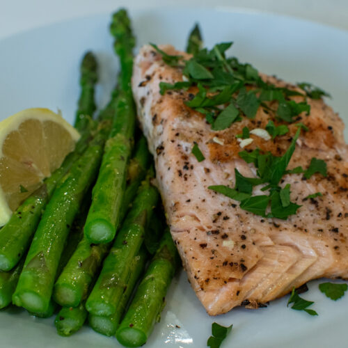 Pan seared salmon fillet with golden crust served over steamed asparagus with lemon wedges