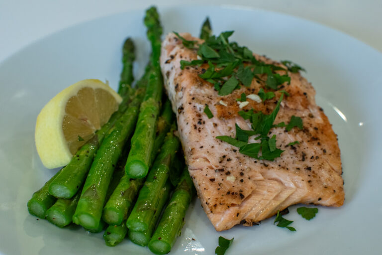 Pan seared salmon fillet with golden crust served over steamed asparagus with lemon wedges